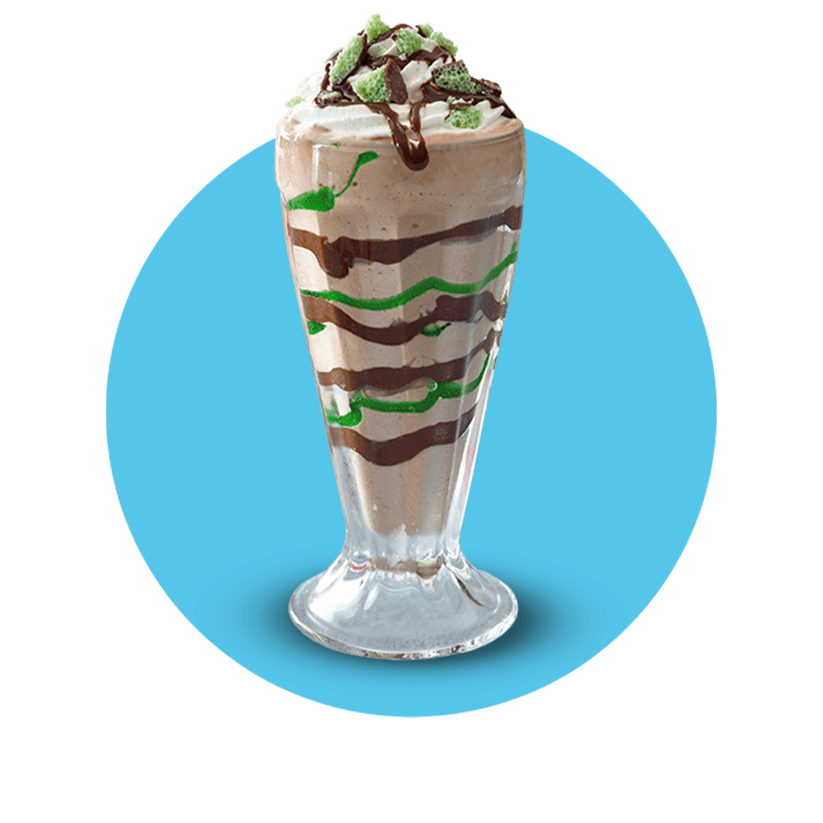 A chocolate milkshake with green sweet sauce and chocolate bits in a transparent glass.
