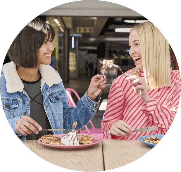 2 ladies toasting with their utensils while enjoying waffles