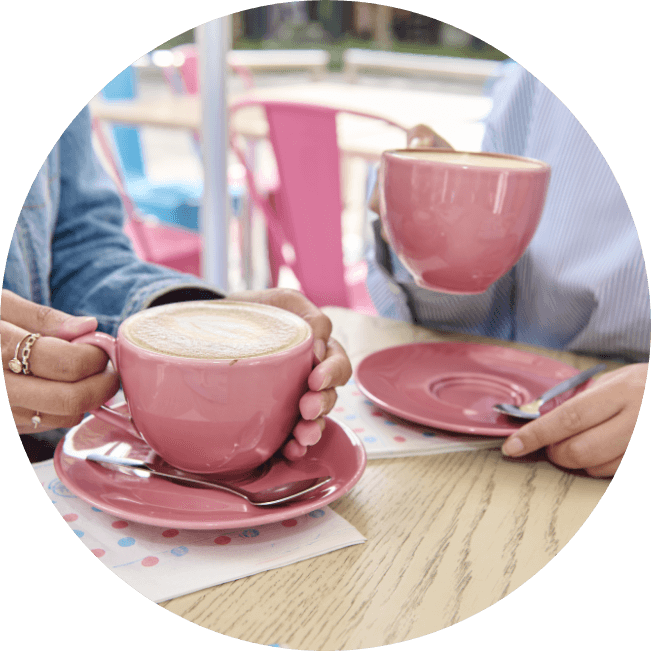 Two people hold pink mugs of cappuccino at an outdoor cafe table